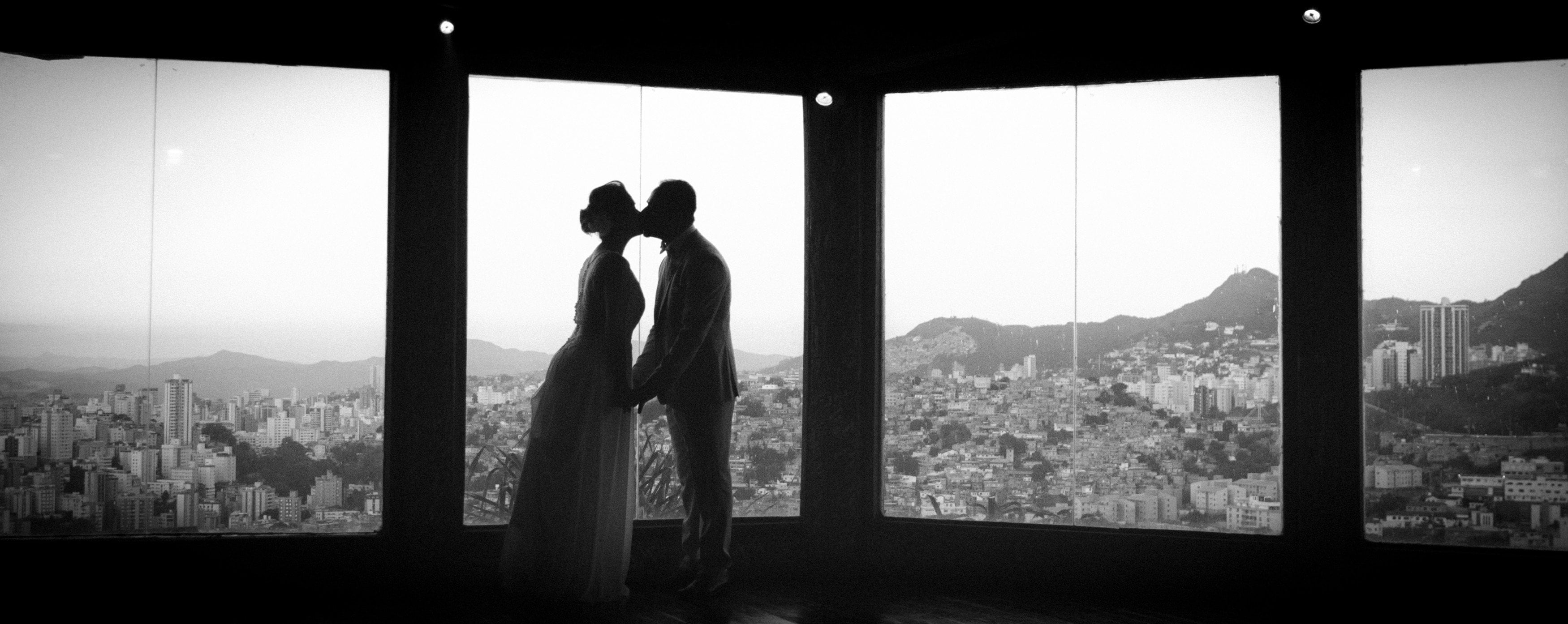 Casal de noivos em silhueta diante de janelas com vista panorâmica da cidade
